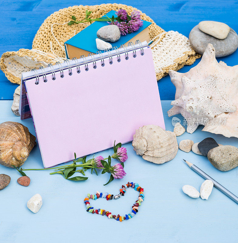 Sketchbook Mock up. Summer sea vacation mockup background. Notebook blank page mock-up with Travel and vacation items on blue wooden table. Sea shells, sea pebbles, clover flowers, straw hat, book